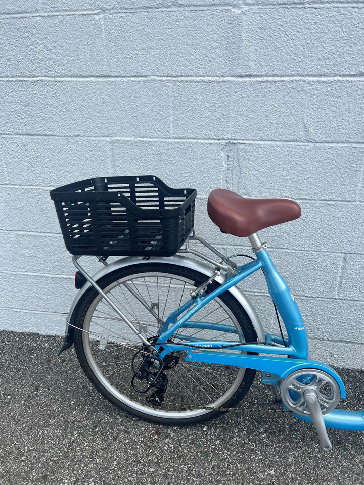 Plastic bike basket attached to rear wheel of bike with white brick wall in background