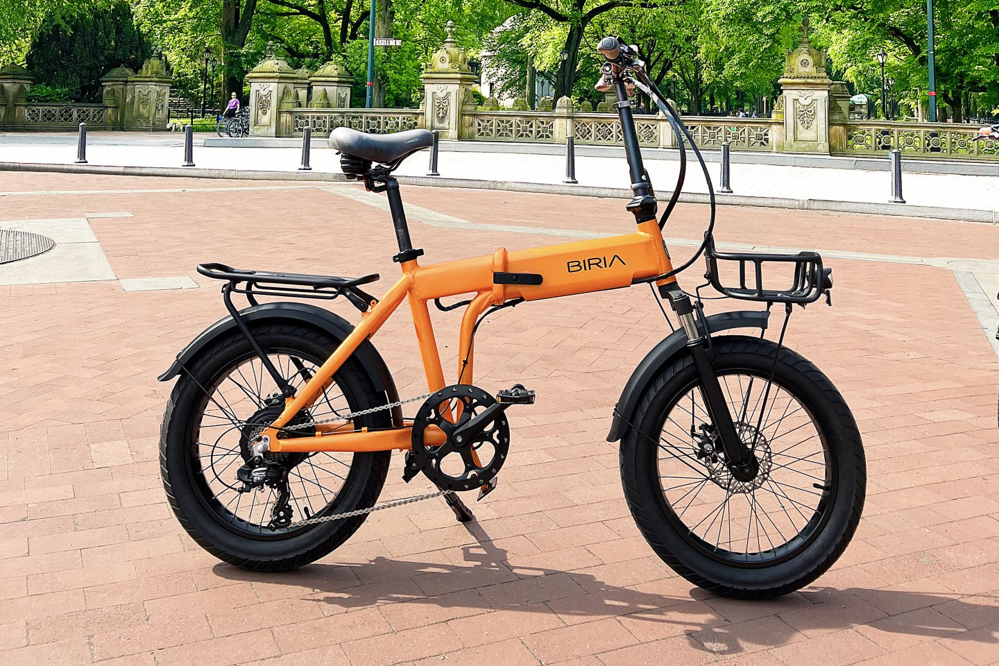 An electric bicycle on a brick road with a sidewalk and park behind it