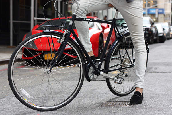 A bicycle being ridden by a man on asphalt. The image is from the waist down.