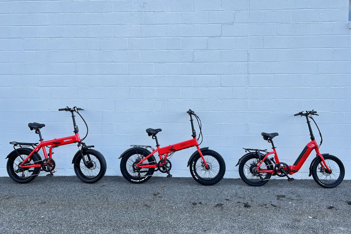 Three bicycles on gravel in front of a white stone wall